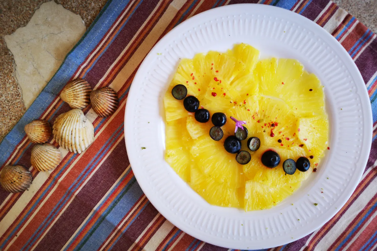 Carpaccio de piña natural macerada en agua de coco con arándanos frescos, postre digestivo tropical ligero